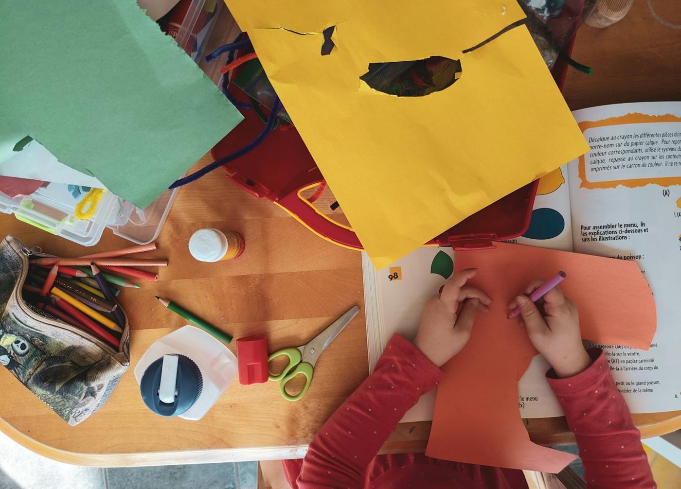 A child cuts and arranges colored paper at a wooden table