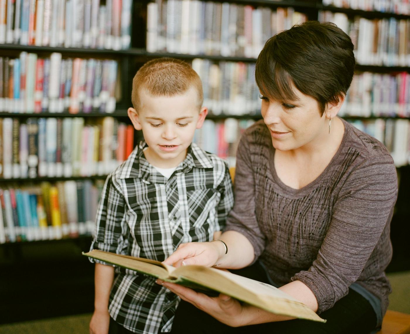 A guide reads a picture book with a young boy in the school library