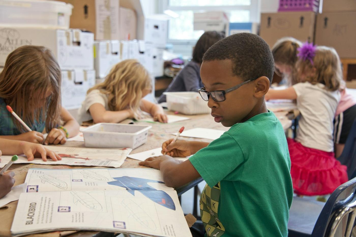 A boy in a green sweater writes at a classroom table