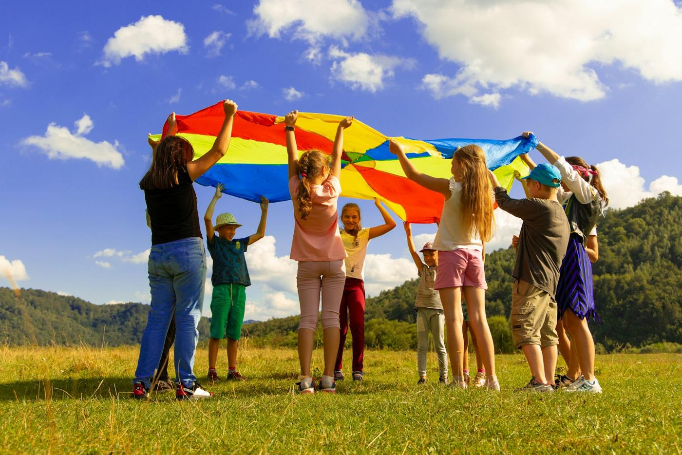 Children lift a rainbow parachute on a sunny field